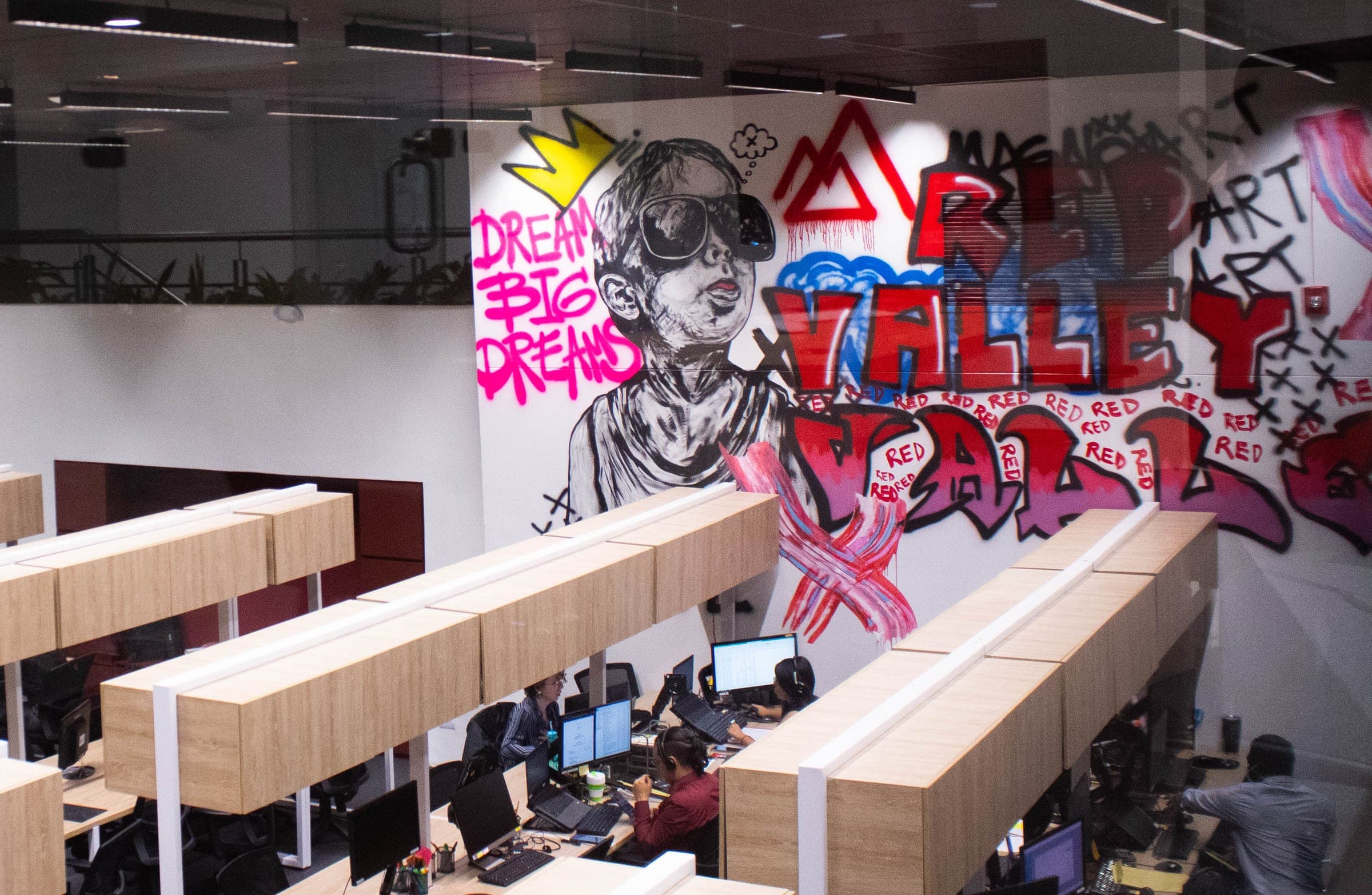 Open workspace with rows of desks and a large Red Valley mural